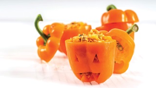 Stuffed orange peppers with carved out Halloween style spooky faces on the front